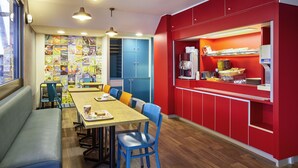A dining area with a long wooden table, blue chairs, and a red counter with a coffee machine. - hotelF1 Paris Saint-Denis Université (Saint-Denis)