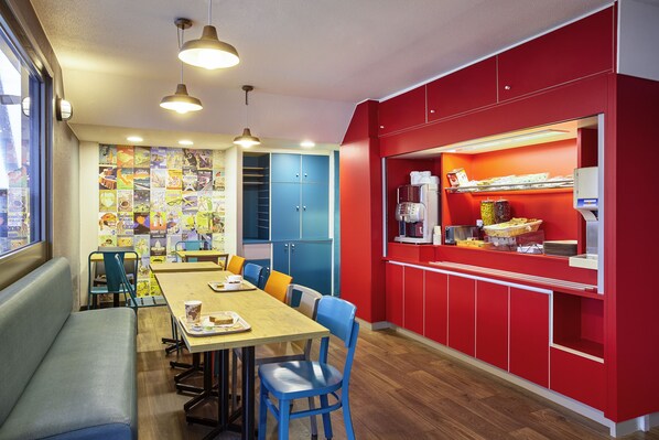 A dining area with a long wooden table, blue chairs, and a red counter with a coffee machine. - hotelF1 Paris Saint-Denis Université (Saint-Denis)