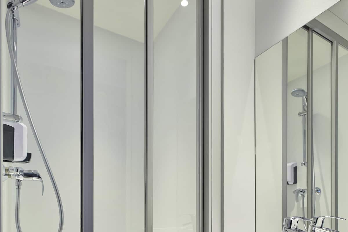 Een moderne badkamer met een douchecabine van glas, een handdouche en een wandmengkraan.