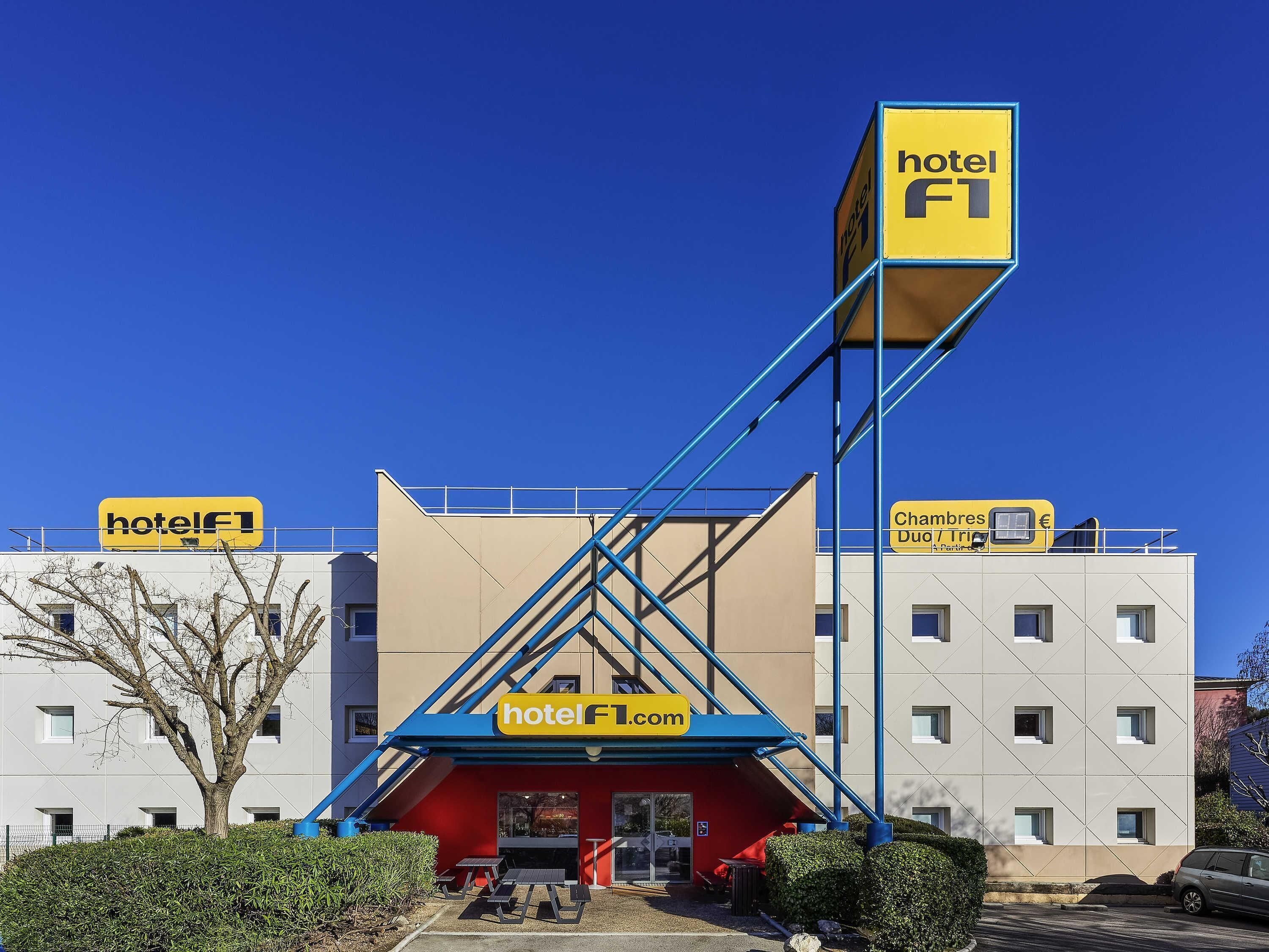 A hotel with a distinctive blue and red entrance, a clear sky, and a parking area.