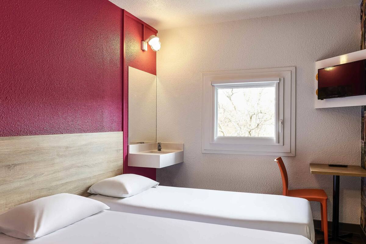 A hotel room with a bed, a window, a sink, and a TV.