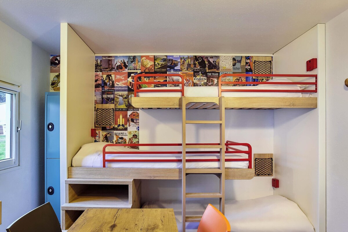 Habitación con literas, un escritorio, una silla, una ventana y una pared decorada con carteles de viajes.