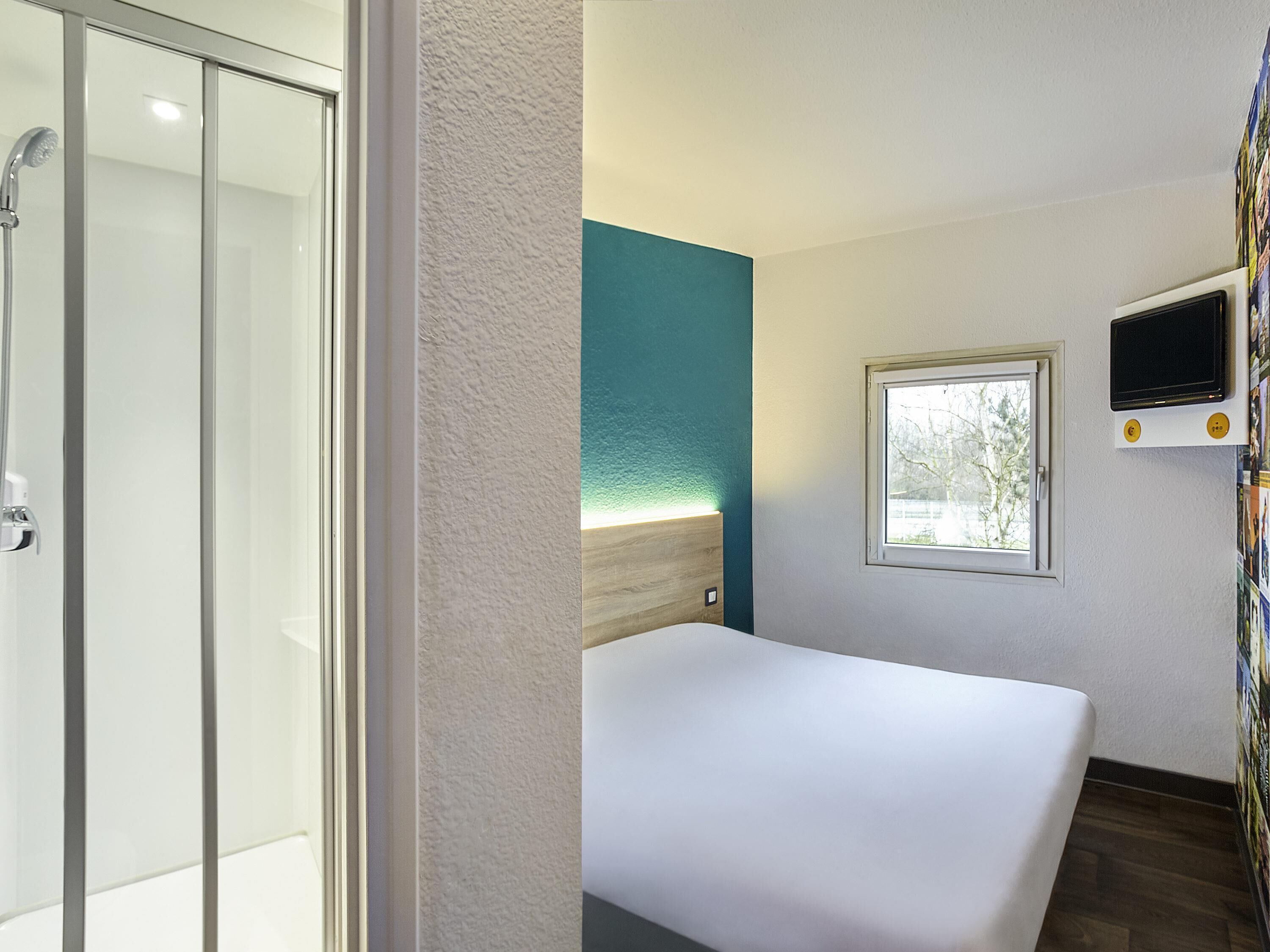 Ein Hotelzimmer mit Bett, Dusche, Fenster und Fernseher.