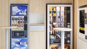 A vending machine with a variety of snacks and drinks, a small table, and a display of packaged goods.