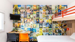 A room with a bunk bed, a desk with a chair, a TV, and a wall covered with travel posters.