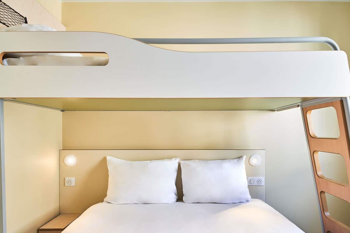 A bunk bed with a headboard, two pillows, a bedside table, and a wall socket.