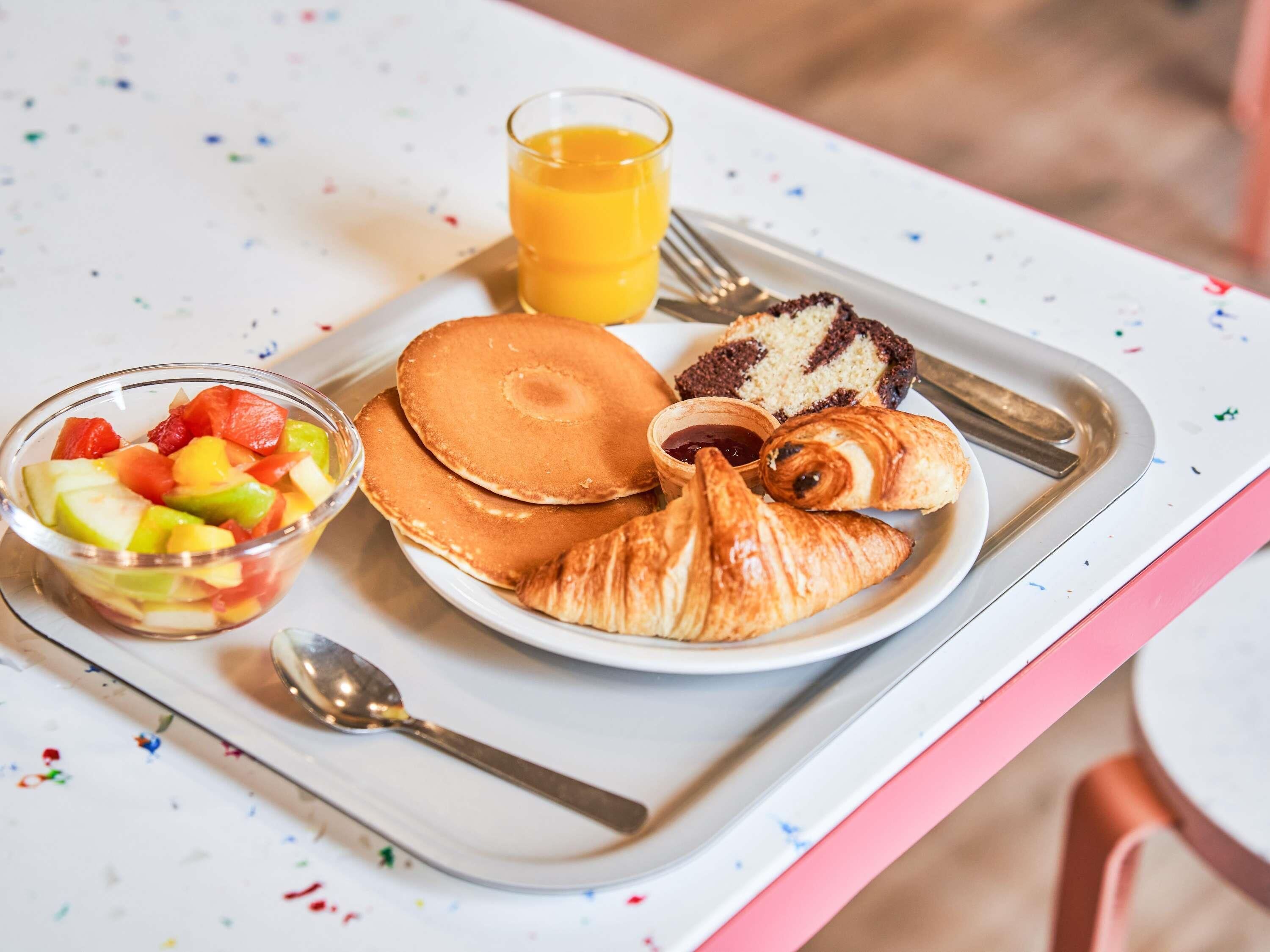 A breakfast tray with pancakes, croissants, a fruit bowl, and a glass of orange juice.