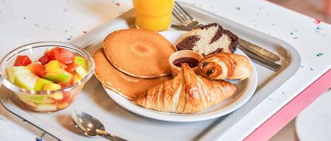 A breakfast tray with pancakes, croissants, a fruit bowl, and a glass of orange juice.