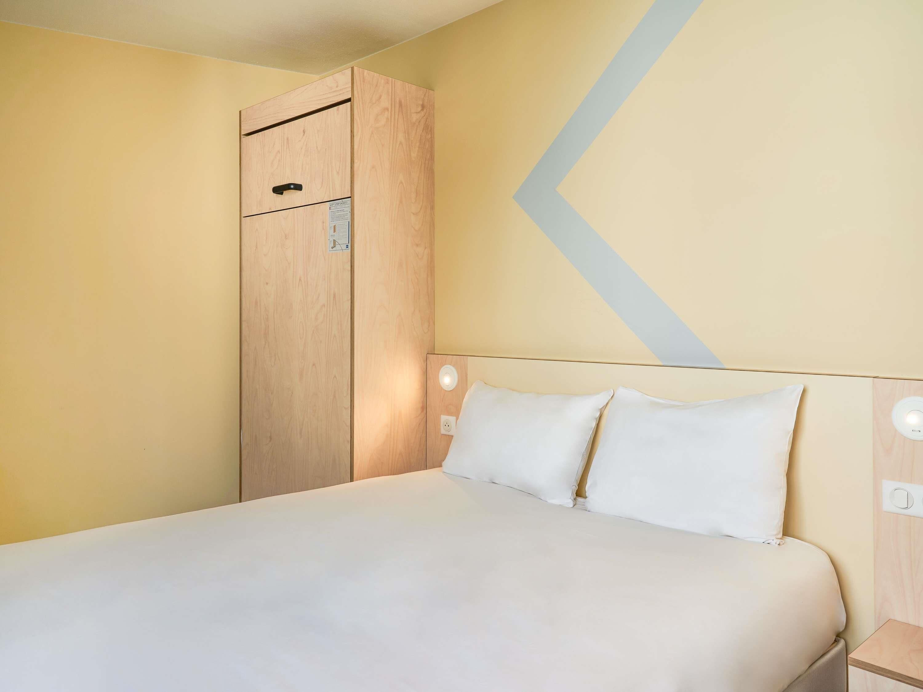 Une chambre d’hôtel avec un lit, une armoire en bois, une lampe fixée au mur et un élément décoratif mural.