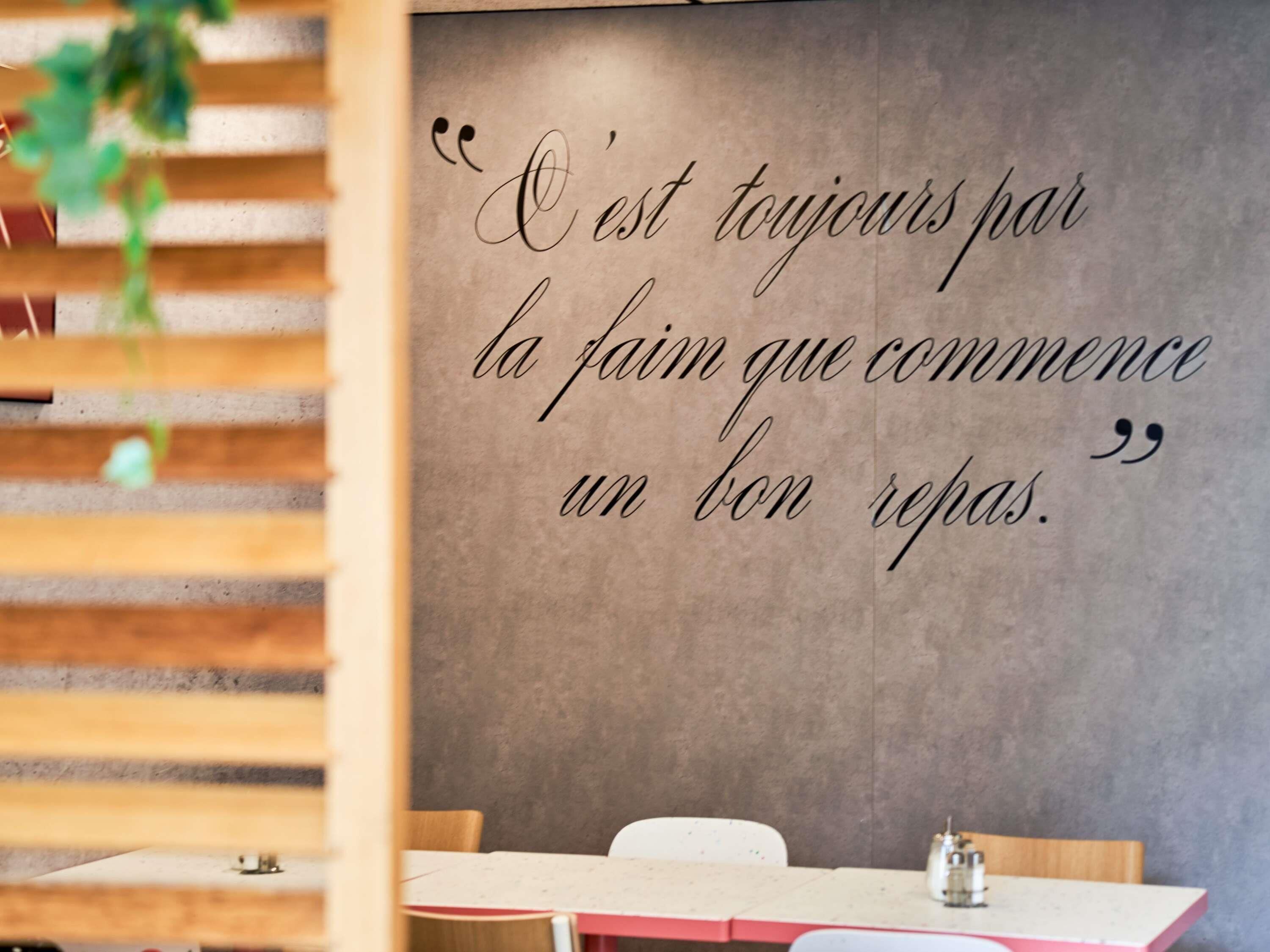 A wall with a quote in French, a table with chairs, and a hanging plant.