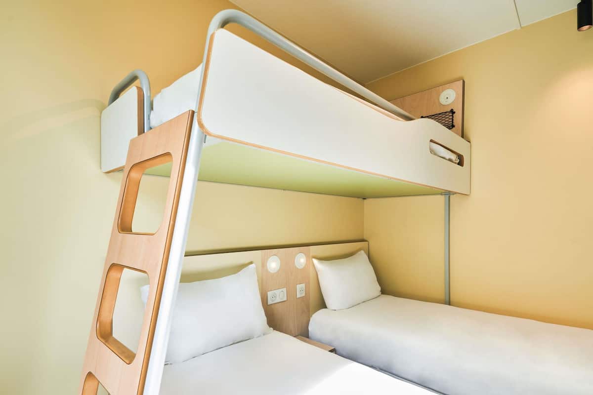 A bunk bed with a ladder, a bedside table, and a wall-mounted light fixture.