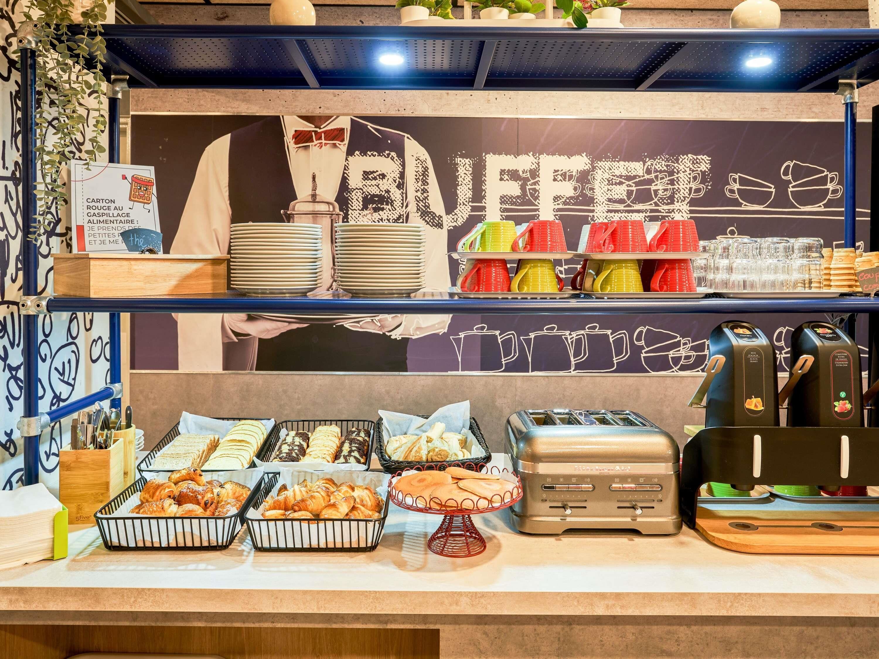A buffet counter with various food items, plates, and cups.