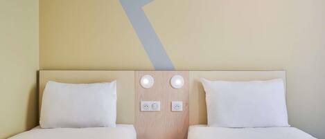 Ein Hotelzimmer mit zwei Betten, einem hölzernen Kopfteil, zwei Wandleuchten und einem kleinen Nachttisch.