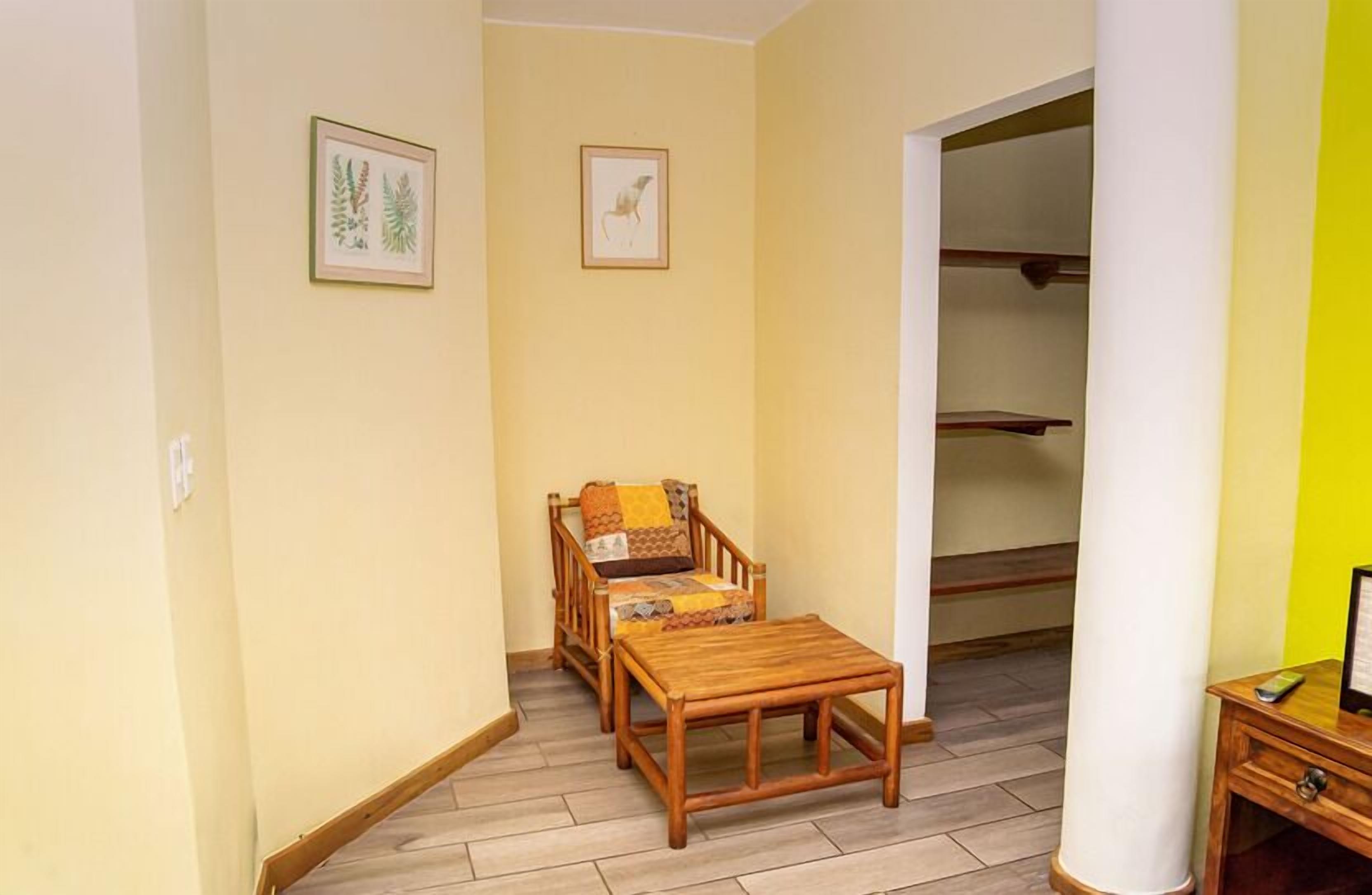 Une pièce avec une table et des chaises en bois, un lit recouvert d’une couverture à motifs et une armoire avec des étagères.
