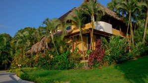 A resort with a thatched-roof building, lush tropical vegetation, and a clear blue sky. - Banana Palms Hotel (Livingston)