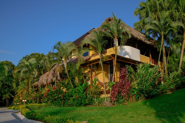 A resort with a thatched-roof building, lush tropical vegetation, and a clear blue sky.