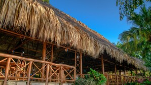 A thatched-roof structure with wooden beams and a lattice wall, surrounded by lush tropical plants. - Banana Palms Hotel (Livingston)