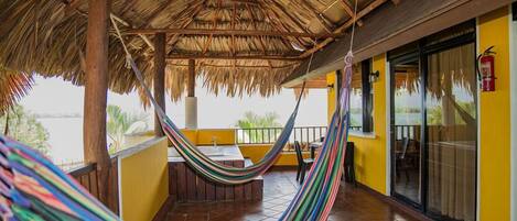 A hammock on a balcony with a view of the water, a fire extinguisher, and a tiled floor.