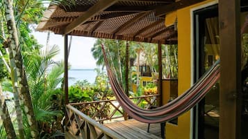 Um deck de madeira com uma rede, cercado por vegetação tropical exuberante e vista para o oceano.
