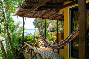 Una terraza de madera con una hamaca, rodeada de exuberante vegetación tropical y vista al océano.