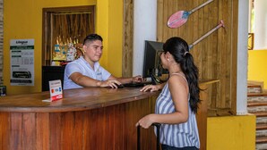 A reception desk with a wooden counter, a computer, and a sign indicating a nearby dance event. - Banana Palms Hotel (Livingston)