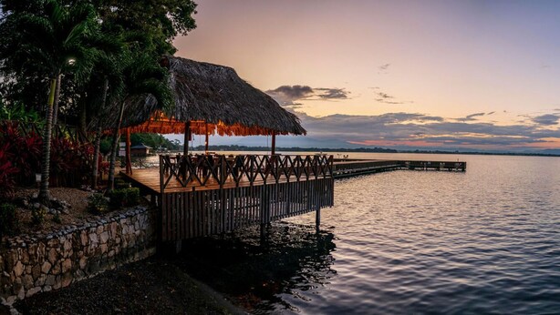 A wooden pier extending into calm waters, a thatched-roof structure, and a stone wall. - Banana Palms Hotel (Livingston)