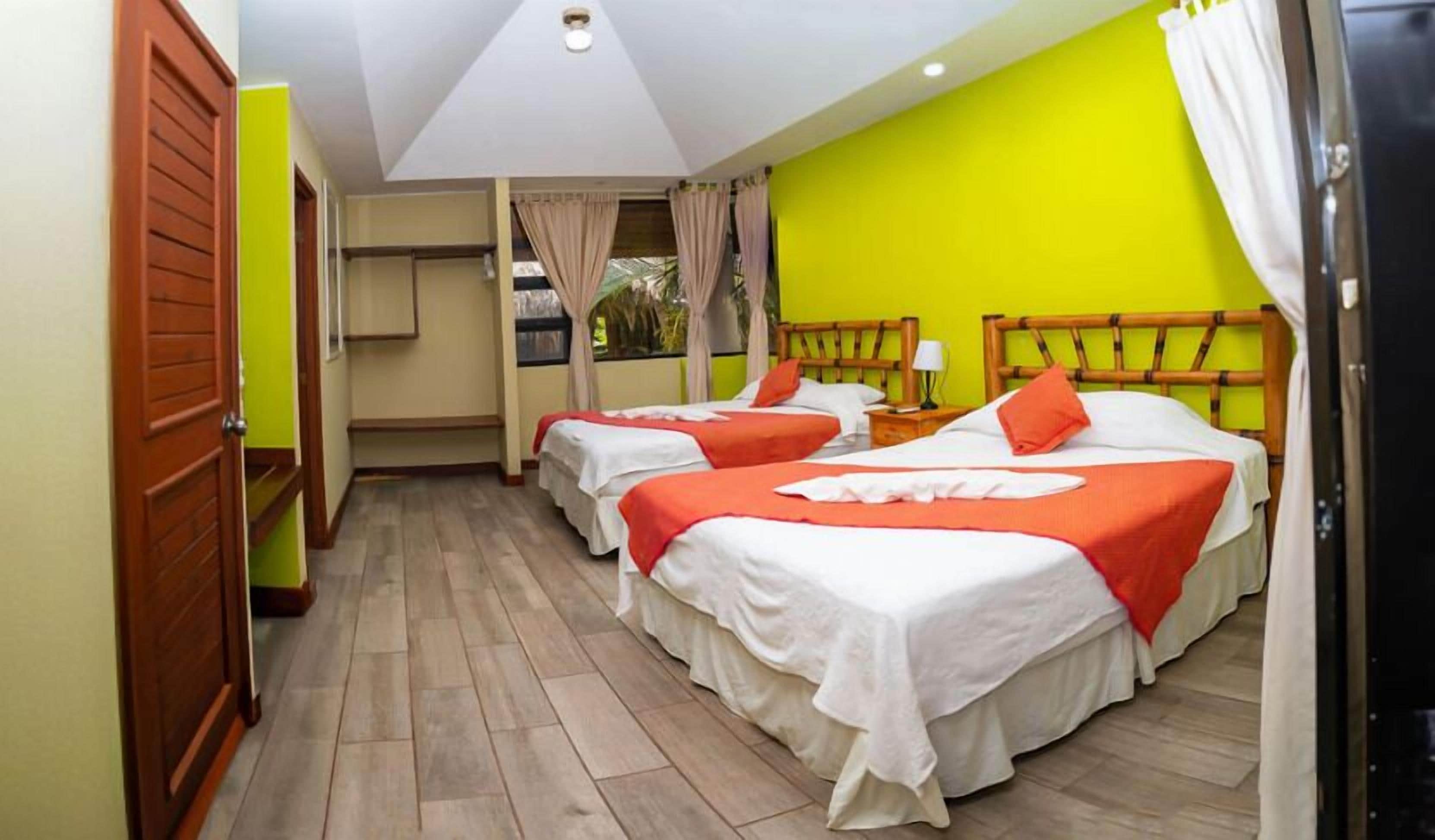 Una habitación con dos camas, una puerta de madera y una pared verde brillante.