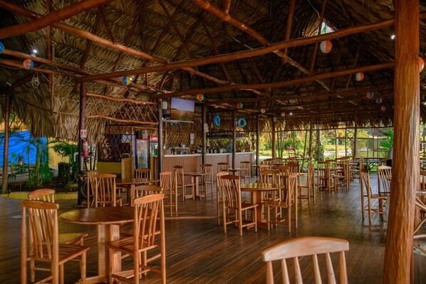 Un restaurante con mesas y sillas de madera, techo de paja y vistas al exterior.