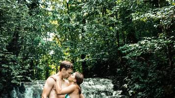 Una pareja abrazándose frente a una cascada en un área boscosa.