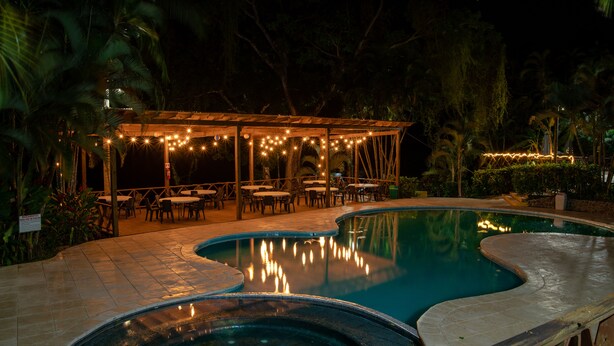 A nighttime outdoor pool area with a covered seating area and string lights. - Banana Palms Hotel (Livingston)