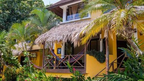 A yellow building with a thatched roof, surrounded by lush greenery and a hammock. - Banana Palms Hotel (Livingston)