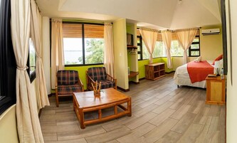 Una habitación con cama, dos sillas, una mesa y un ventanal con cortinas.