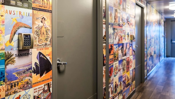 Un pasillo con carteles de viaje antiguos en las paredes, una puerta con lector de tarjeta de acceso y suelo de madera.