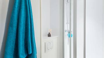 A bathroom with a glass shower enclosure, a towel rack with a blue towel, and a small shelf with toiletries.