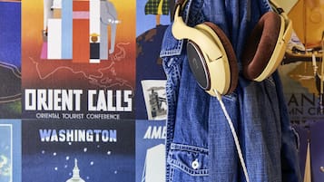 A denim jacket with headphones hanging on a wall with various travel posters.