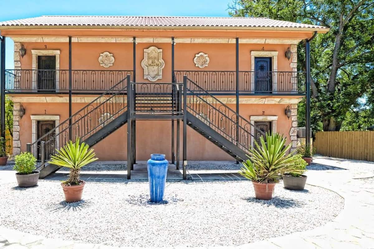 A two-story building with a central staircase, potted plants, and a blue vase in the courtyard.