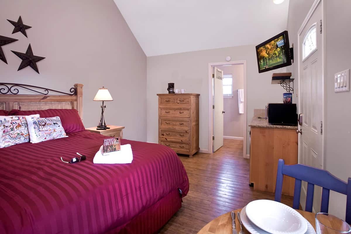 A bedroom with a large bed, a dresser, a television, and a dining area with a table and chairs.