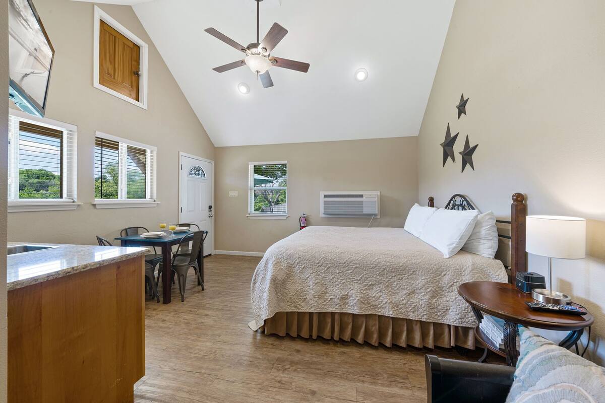A bedroom with a bed, a desk, a chair, a ceiling fan, and a window.