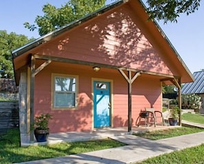 A small pink house with a blue door, a porch, and a window. - Blanco Riverside Cottages & RV (Blanco)