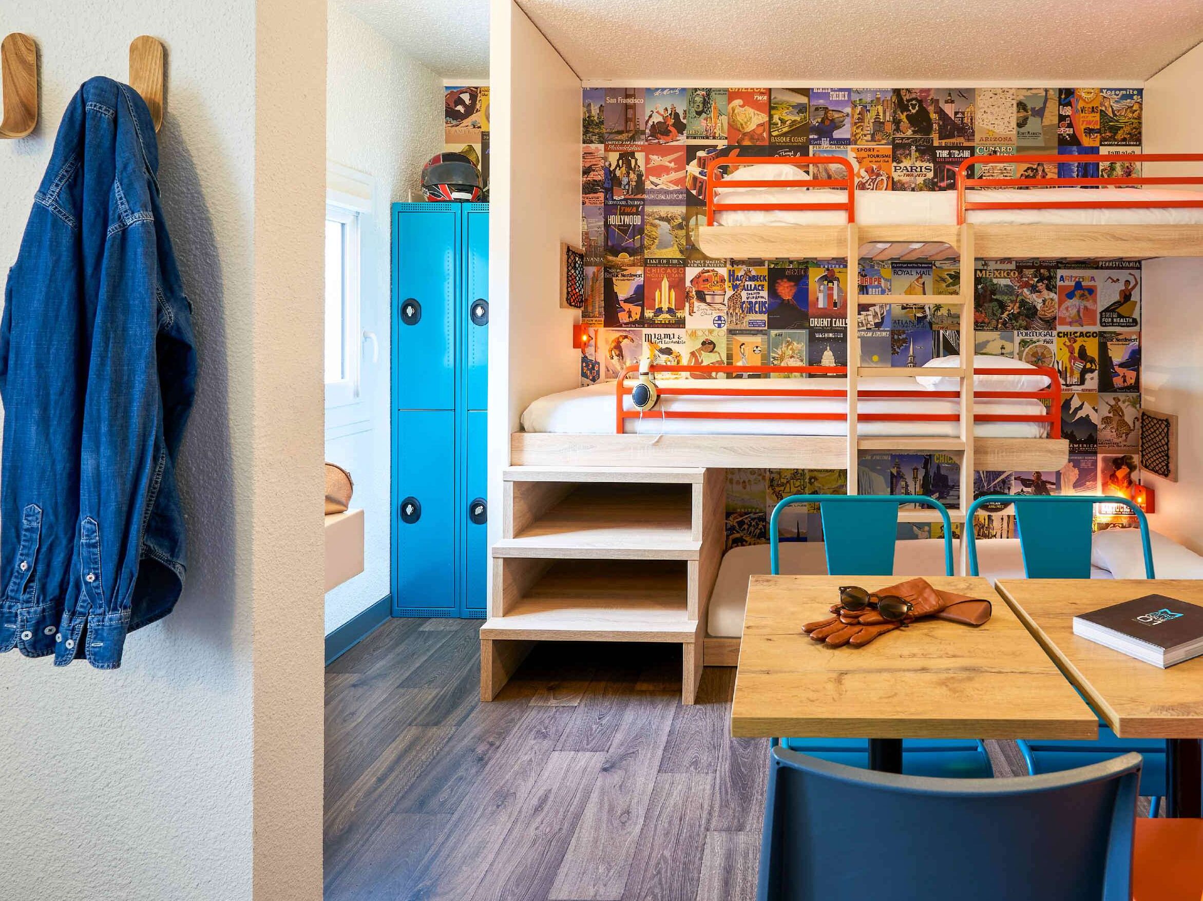 Una habitación con literas, un escritorio, sillas y una pared decorada con carteles de viajes.