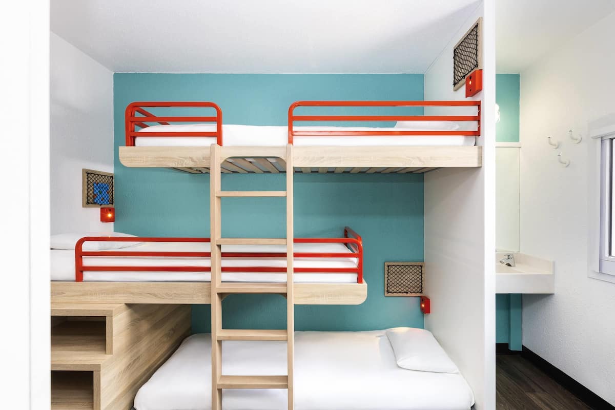 A bunk bed room with a wooden ladder, a small window, and a sink in the corner.