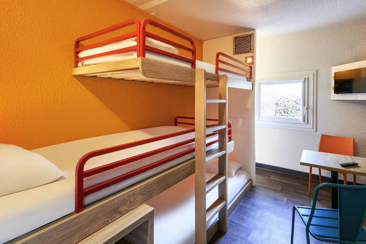 A bunk bed room with a desk and chair, a window, and a wall-mounted air conditioner.
