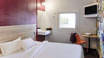 Habitación de hotel con cama, un pequeño escritorio con silla, una ventana y televisor montado en la pared.