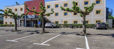 A multi-story hotel with a parking lot, trees, and a red building in the background.