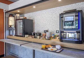 Una barra de desayuno moderna con una máquina de café, un refrigerador y una estación para café.