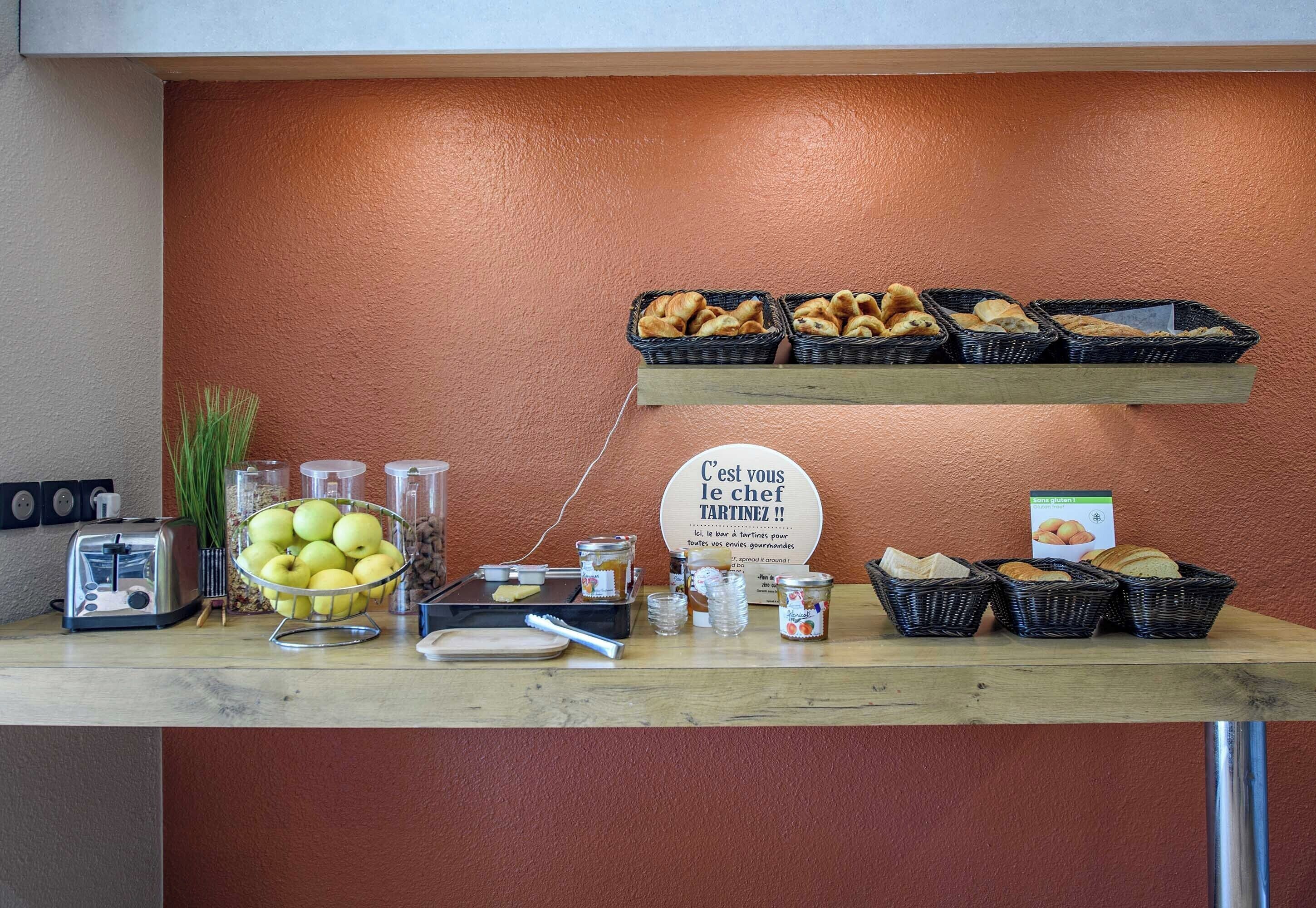 A breakfast bar with bread, pastries, apples, and condiments.