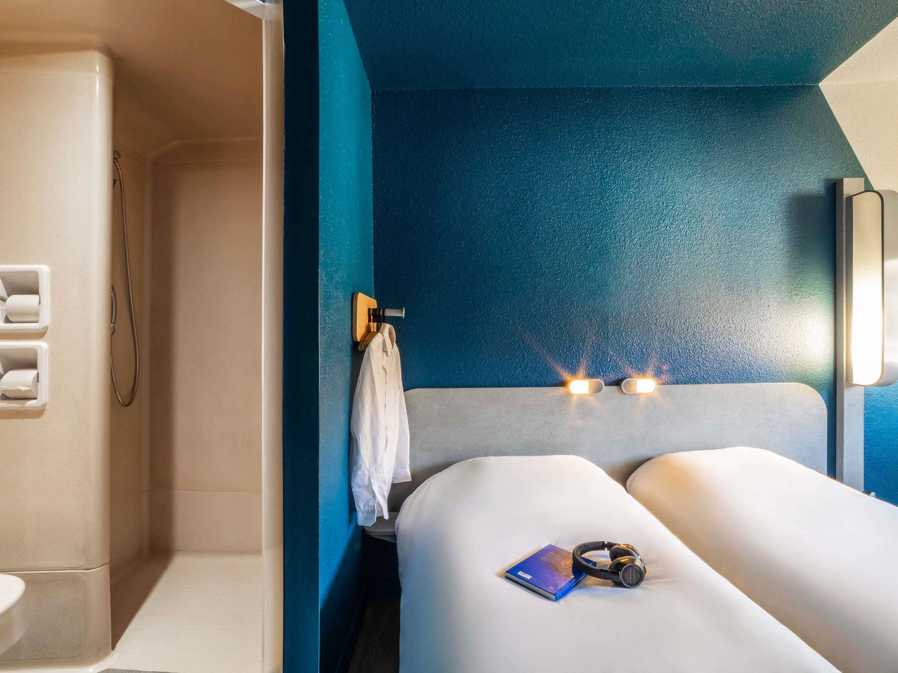 A modern room with a blue accent wall, a bed with a white headboard, a bedside table with a book and headphones, and a towel hanging on a hook.