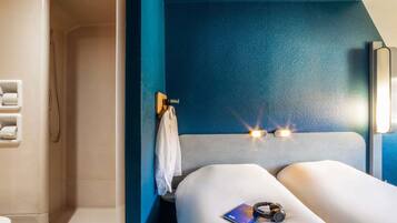 Una habitación moderna con una pared azul de acento, una cama con cabecera blanca, una mesita de noche con un libro y auriculares, y una toalla colgada en un gancho.
