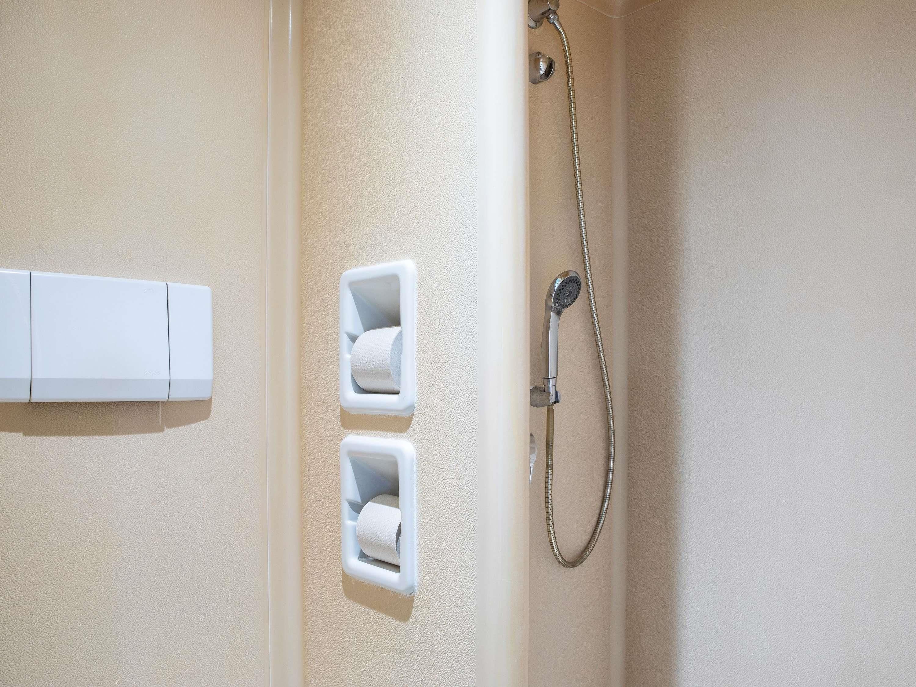 Un baño con ducha, dispensadores de papel higiénico y un perchero para toallas.