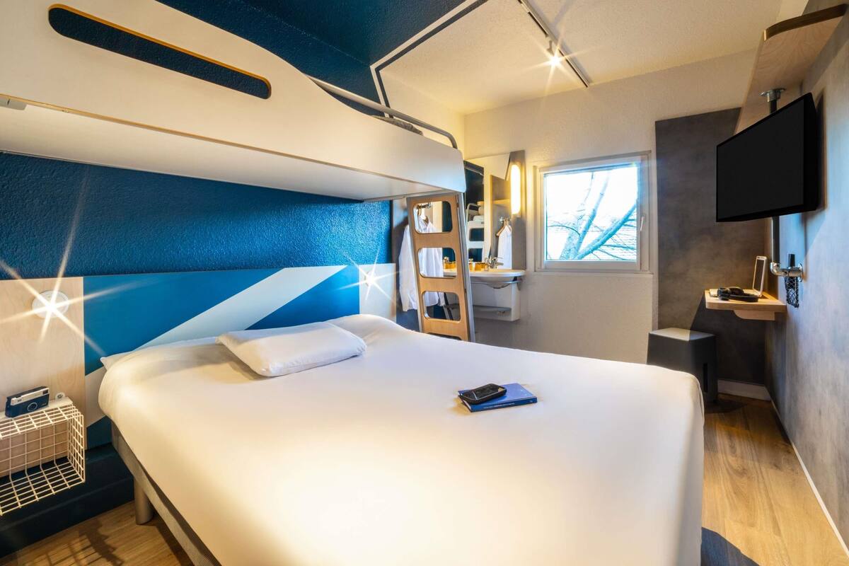 Une chambre d’hôtel moderne dotée d’un grand lit, d’une table de chevet, d’un téléviseur fixé au mur et d’une fenêtre donnant sur l’extérieur.